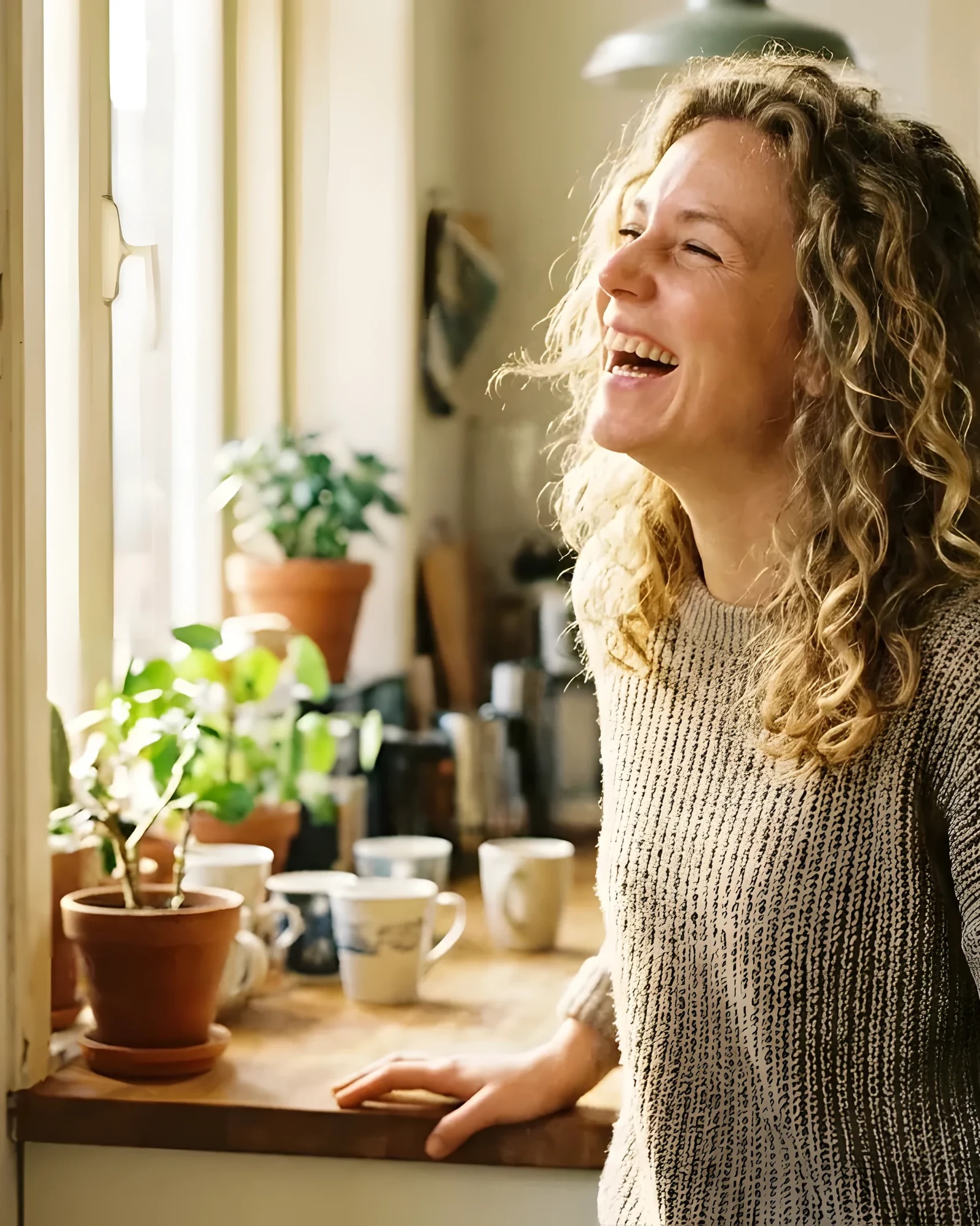 Een vrouw lacht in haar keuken tussen de planten, in de ochtendzon